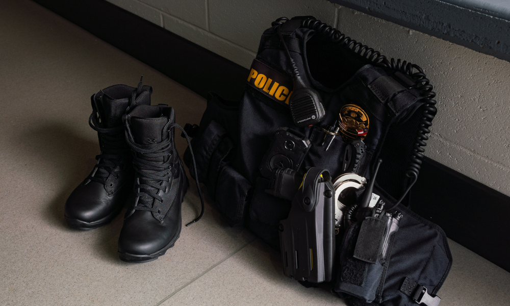Set of police equipment on the floor: Garmont tactical boots, bulletproof vest, radio, badge, handcuffs, and holster