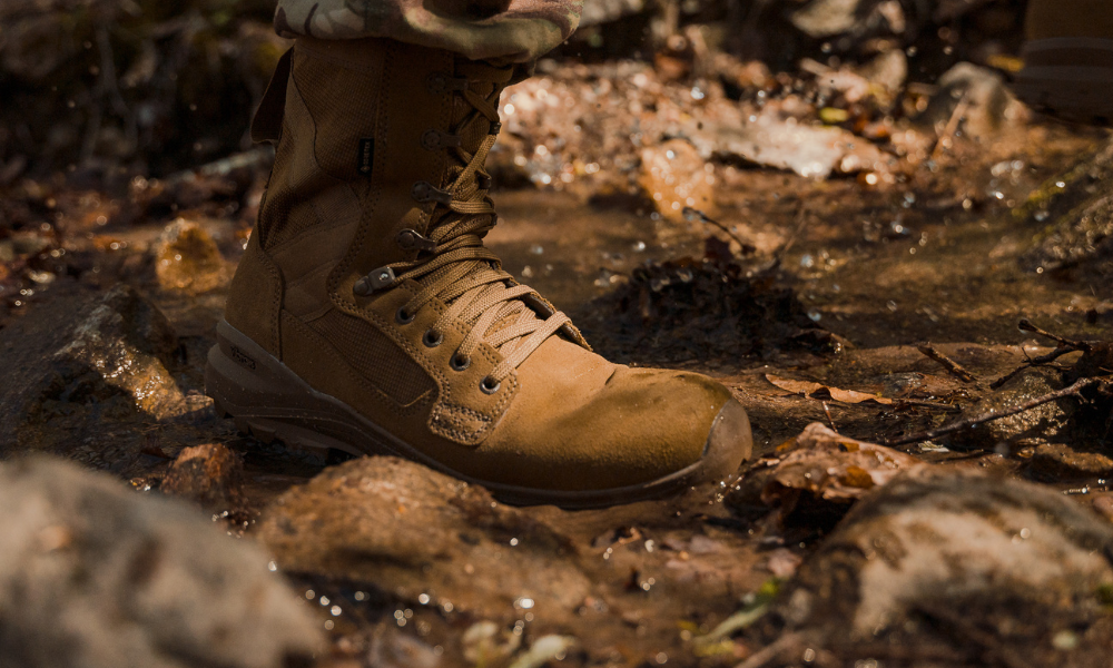 Close-up of Garmont Tactical tan tactical boot stepping into a shallow stream, surrounded by rocks and wet leaves