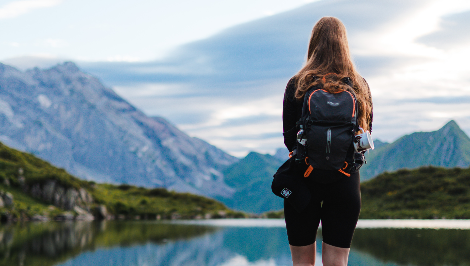 Persona con mochila de espaldas mirando el paisaje de montaña frente a un lago tranquilo