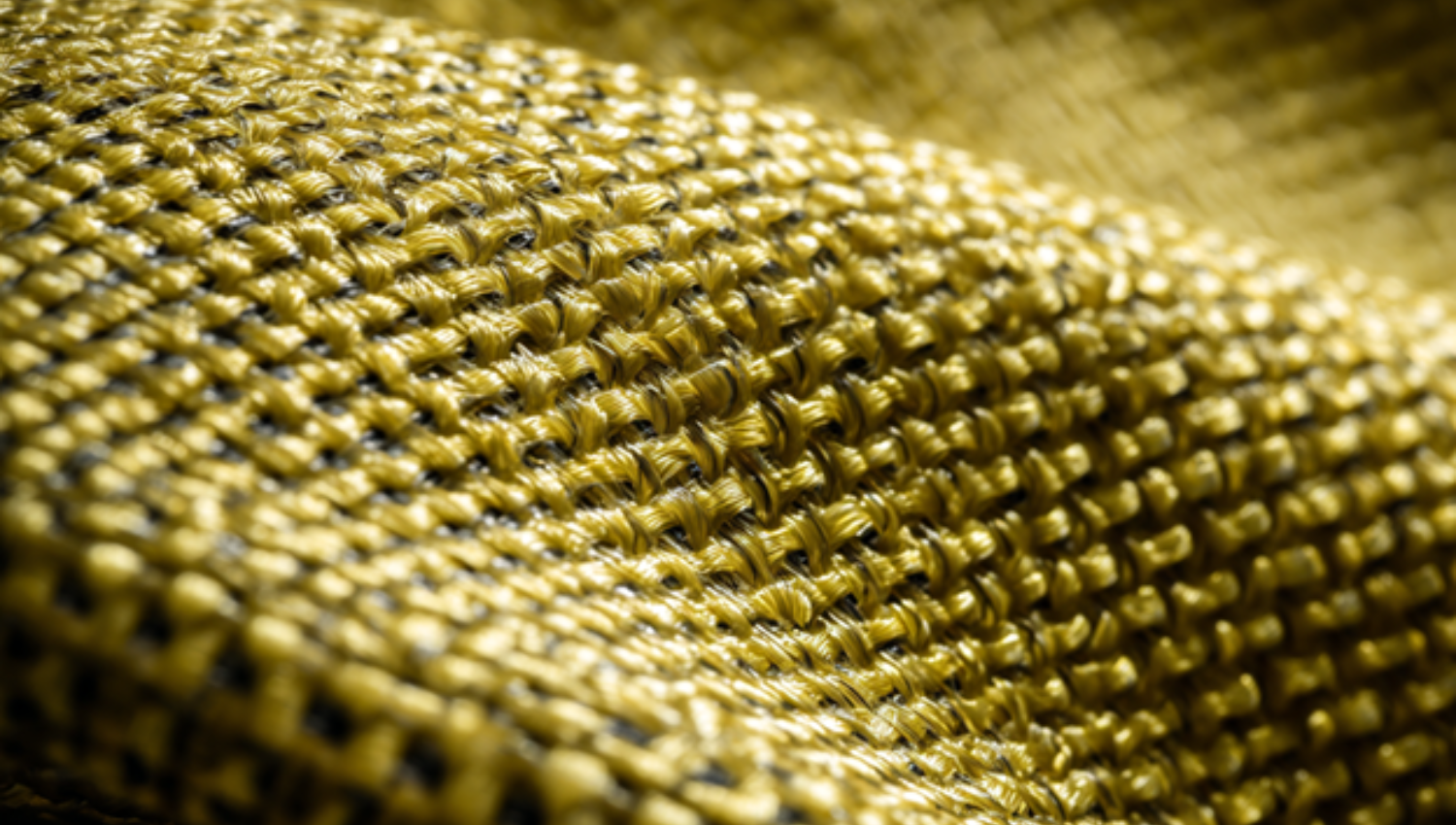 Primo piano della trama intrecciata di un tessuto in Kevlar® giallo, evidenziato da luce naturale