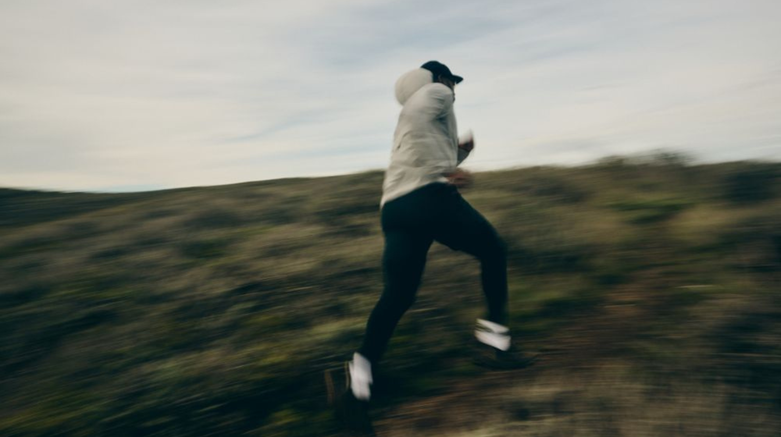 Persona che corre in salita su terreno naturale indossando scarpe Naglev, in un’immagine dinamica e sfocata