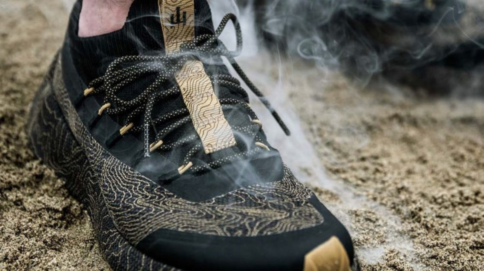 Primo piano di una scarpa Naglev con dettagli in rilievo e fumo scenografico su sfondo sabbioso