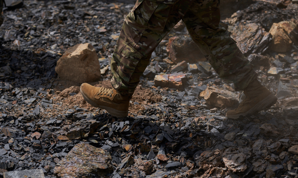 Military wearing camouflage pants and Garmont tactical boots walking over rocky terrain with scattered black shale and stones