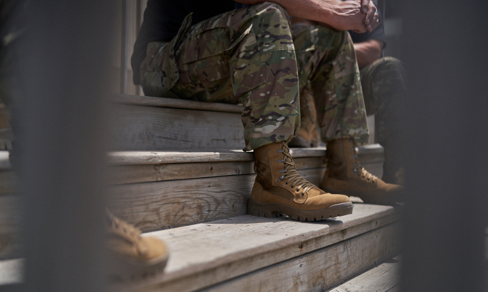 Soldier in camouflage pants sitting on wooden steps, wearing tan tactical boots, partially obscured by a railing