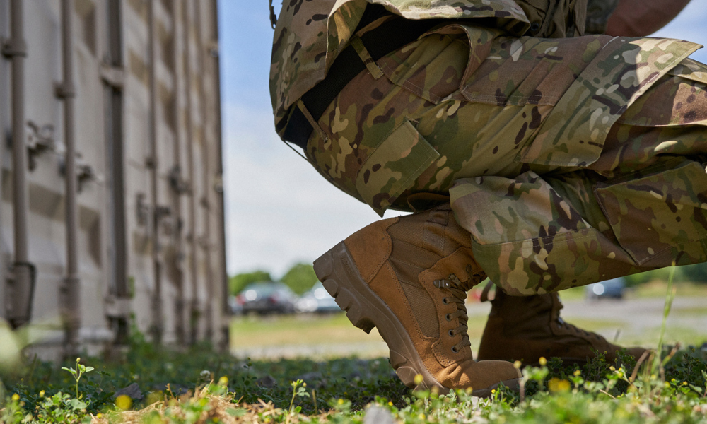 Close-up of a soldier squatting near a container, wearing camouflage uniform and Garmont tactical boots.