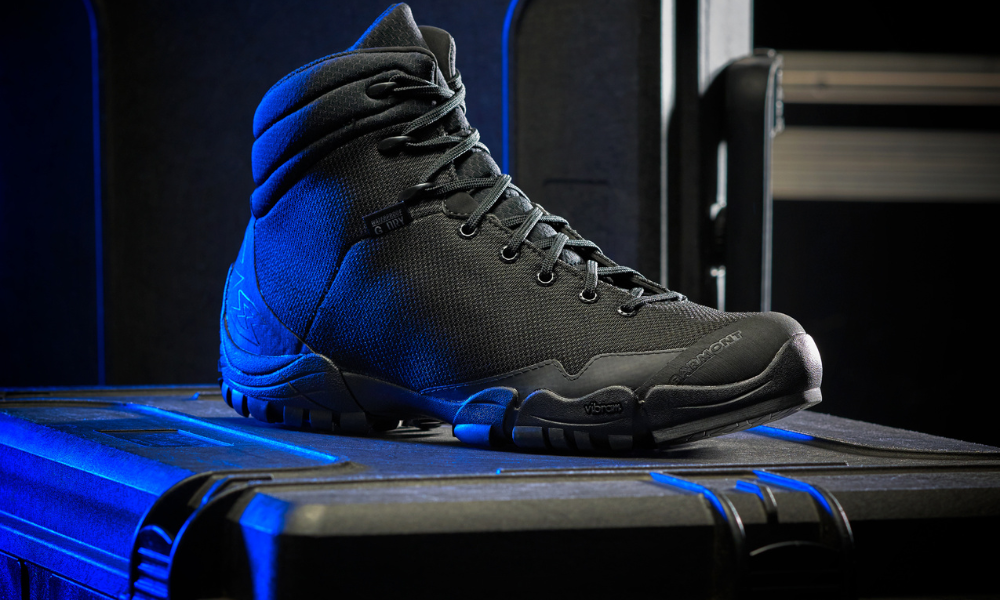 Studio shot of a black Garmont tactical boot with Vibram sole, placed on a hard case under blue lighting.