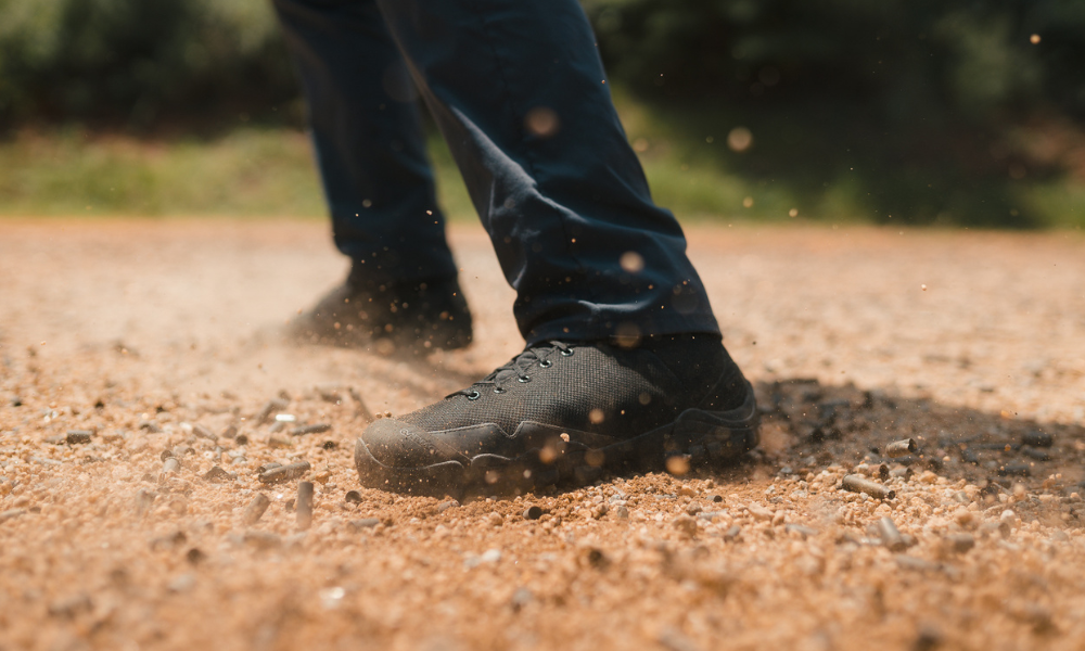 Close-up of black tactical shoes kicking up dust and debris on a gravel surface during movement