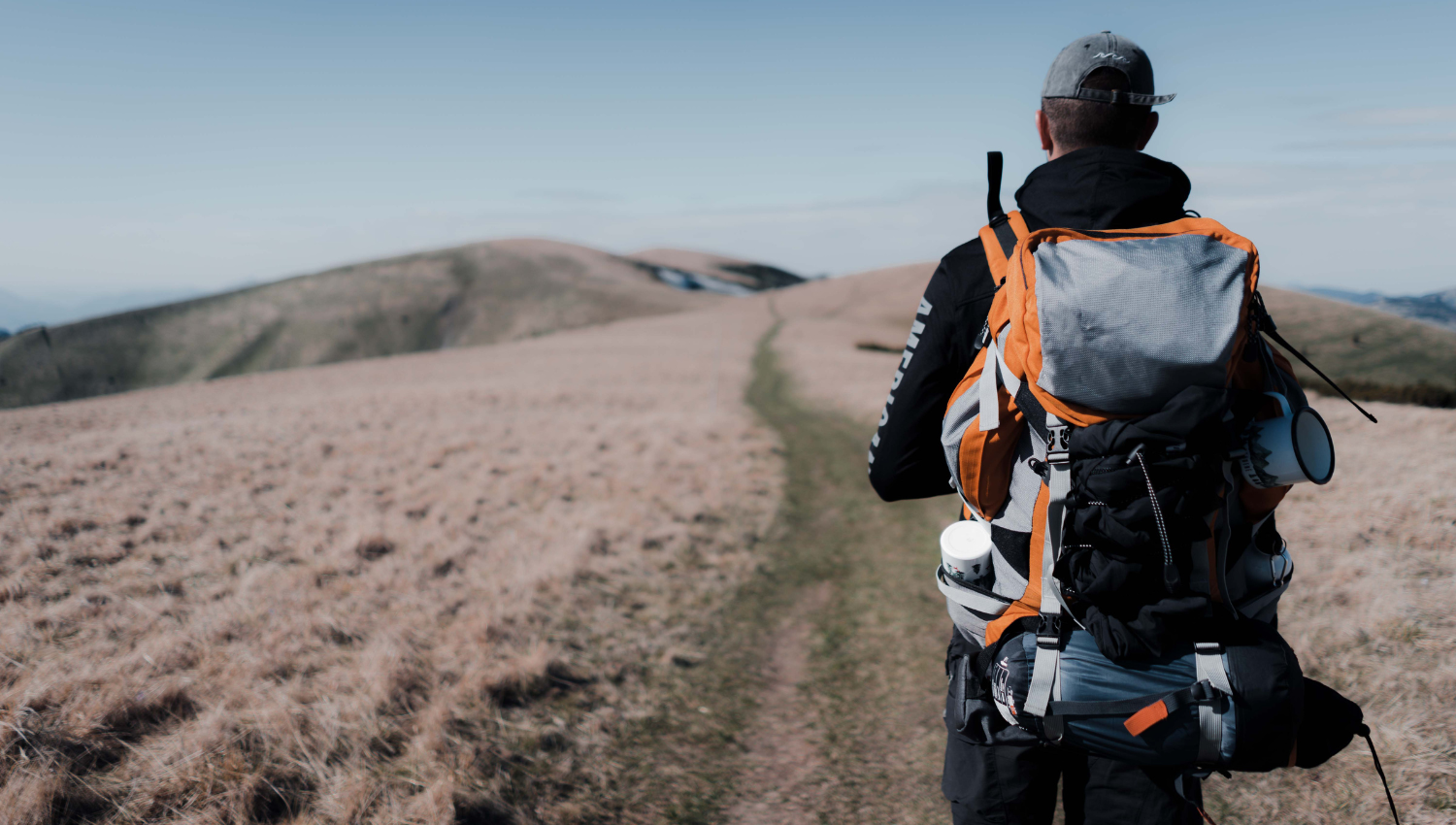 Excursionista caminando por un sendero de montaña con una gran mochila equipada.
