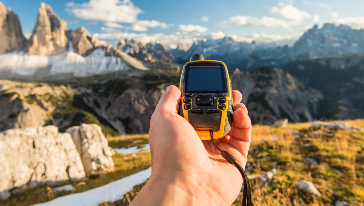 Mano che tiene un dispositivo GPS con le montagne sullo sfondo e cielo parzialmente nuvoloso.