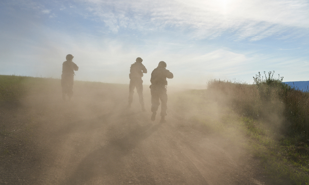 Soldiers walking through a dusty field under a bright sky