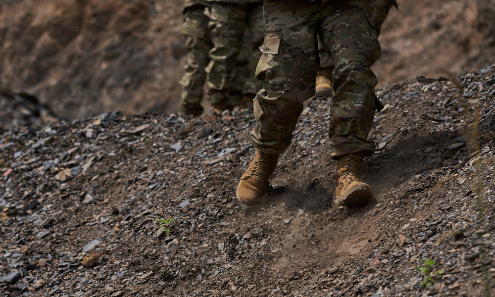 Close-up of soldiers’ tactical boots trekking on rocky terrain