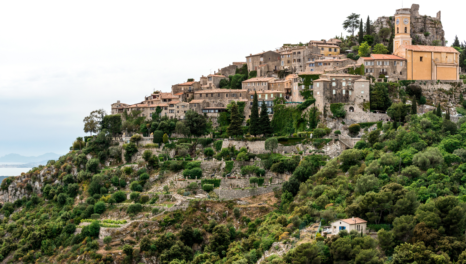 Borgo di Matera su una collina verde con terrazzamenti e vista sul mare sullo sfondo.
