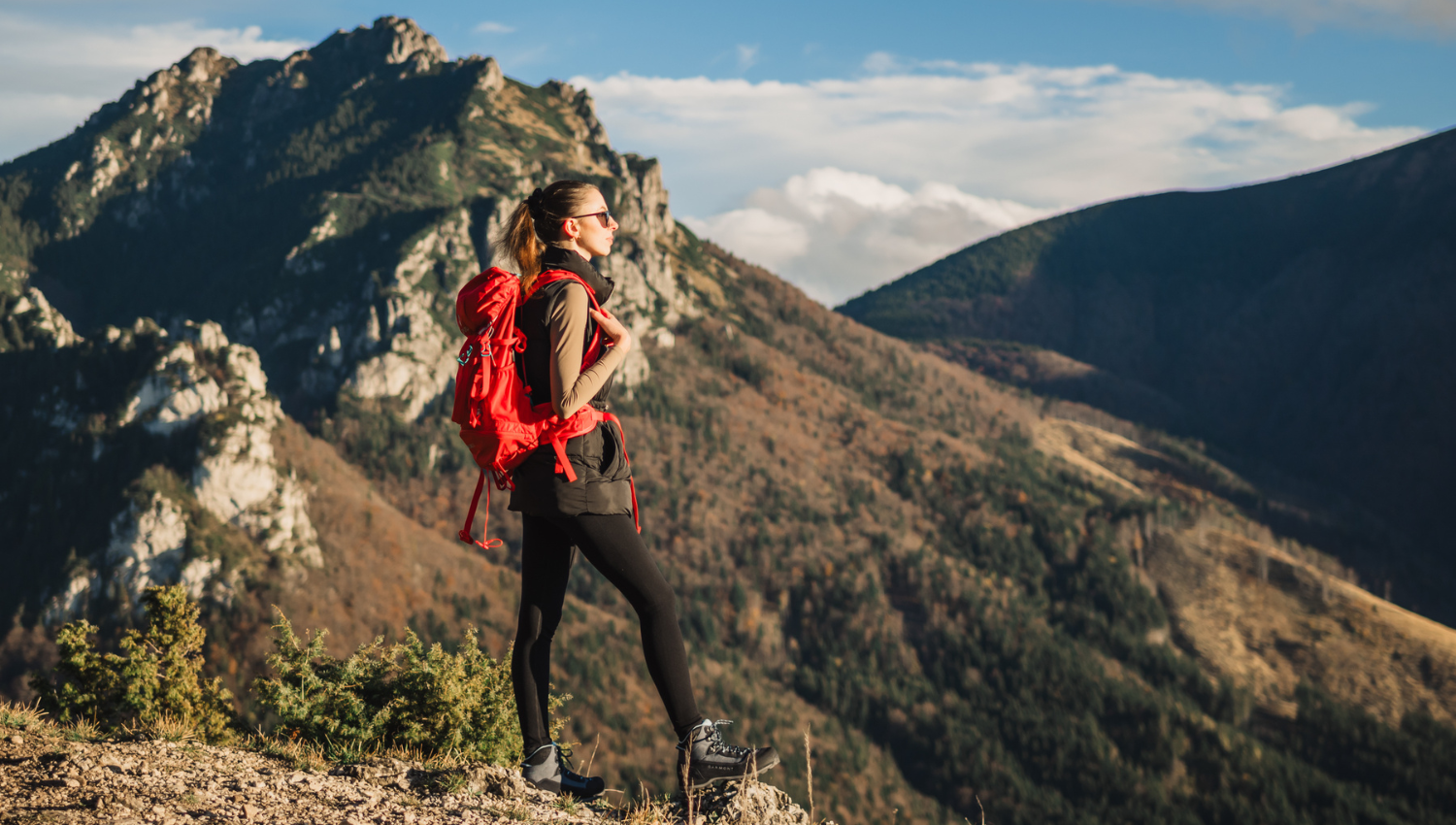 Mujer con mochila roja admirando la vista desde la cima de una montaña.