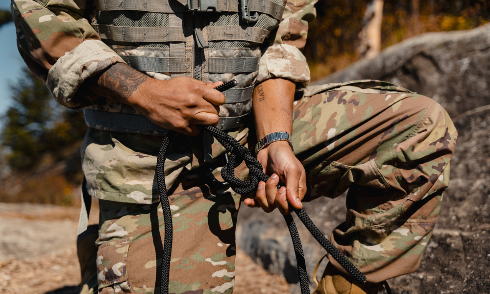 Close-up of hands tying a knot with rope, person wearing camouflage military uniform.