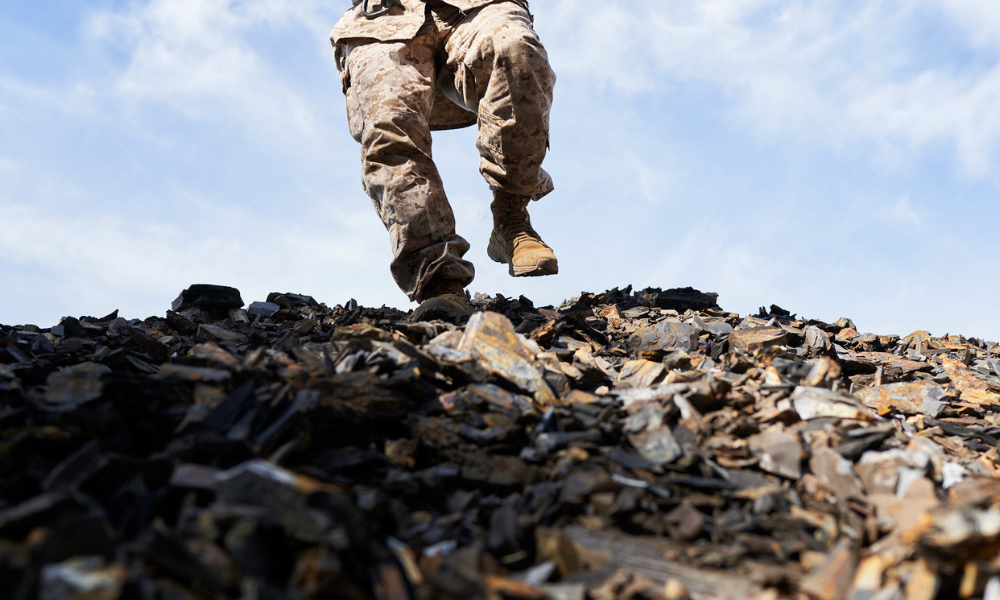 Close-up of soldier jumping on sharp rocks, wearing desert camouflage pants and tan tactical boots.