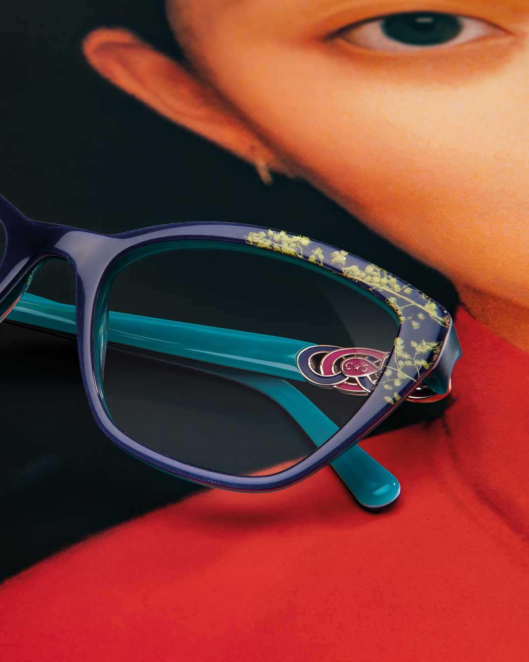 A woman wearing glasses holds a rose in front of a vibrant blue background.