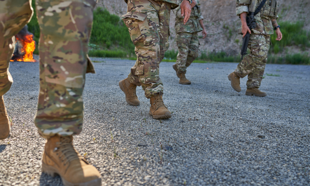 US soldiers in combat uniforms and tactical boots marching on gravel terrain during a training exercise.