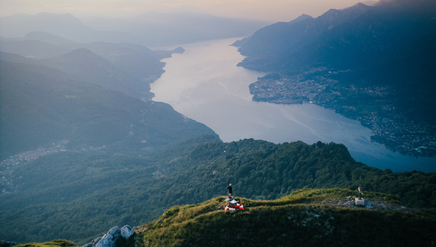 Vista dall’alto del lago di garda circondato da montagne e vallate, con una persona in piedi su un crinale.