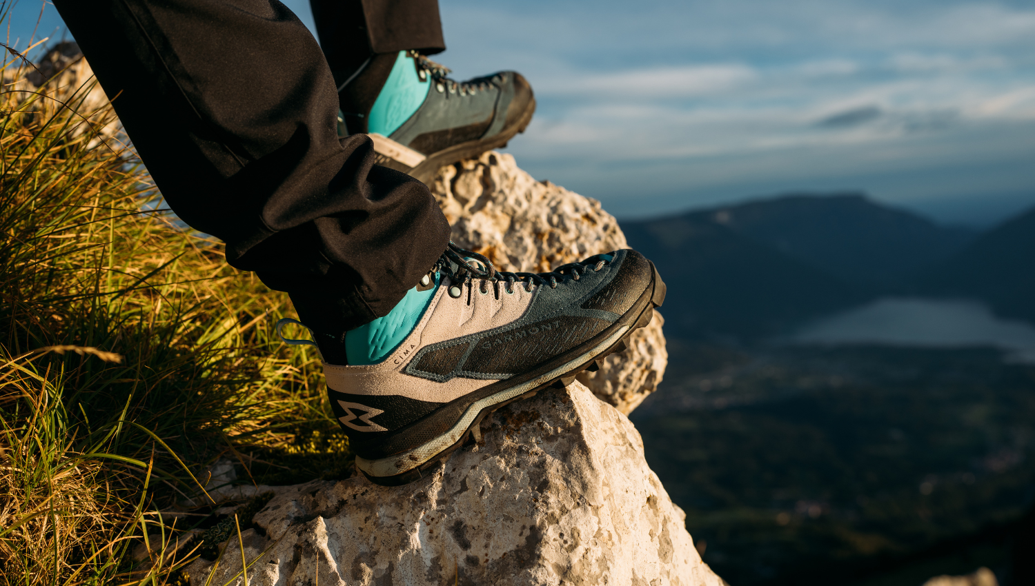 Primo piano di scarponi da trekking garmont appoggiati su una roccia con vista su lago e montagne.