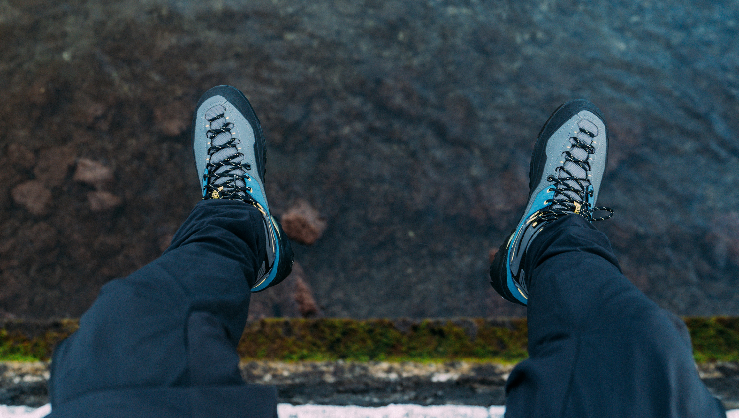 Piedi con scarponi da trekking garmont sospesi sopra l’acqua, visti dall’alto su un bordo roccioso.