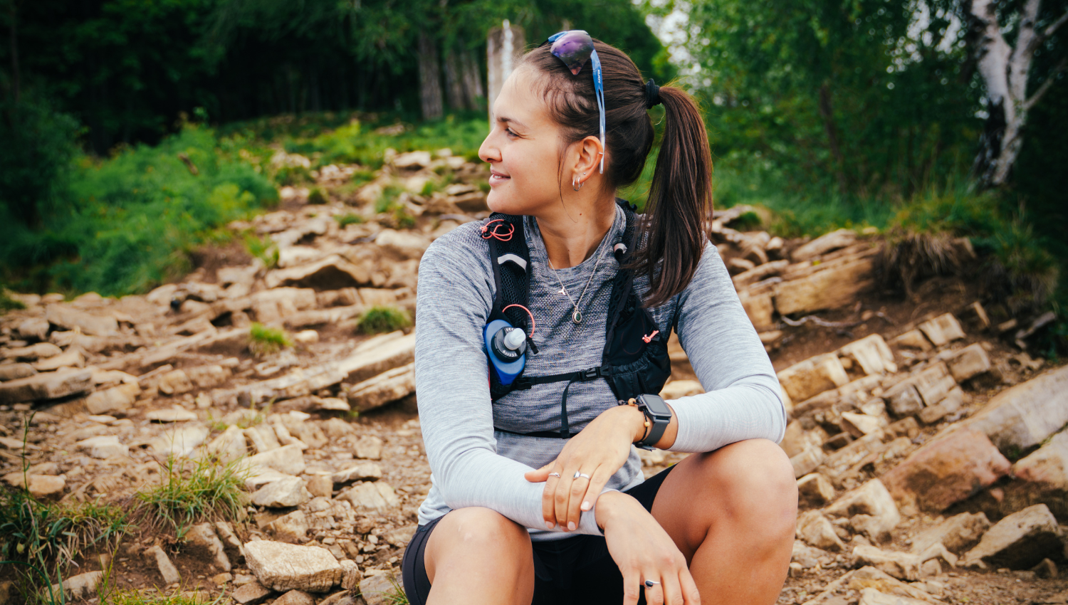 Mujer con ropa técnica sentada en un sendero rocoso, descansando y mirando hacia un lado durante una caminata.