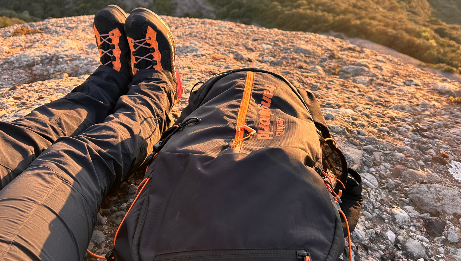 Mochila de senderismo y botas apoyadas sobre roca, iluminadas por la luz cálida del atardecer en la montaña.
