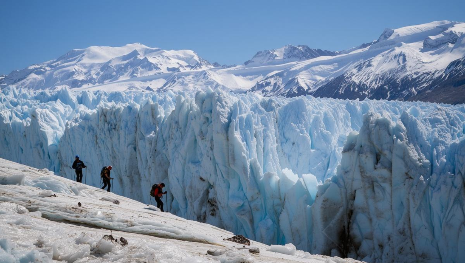 Excursionistas caminando sobre el glaciar Perito Moreno con grietas de hielo y montañas nevadas alrededor.