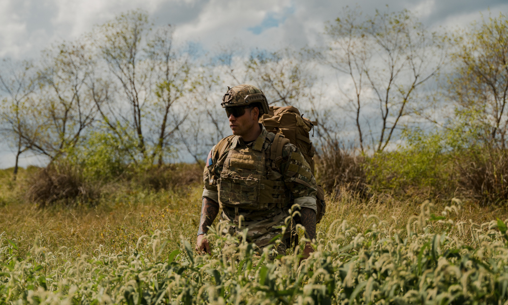     Soldier wearing full tactical gear and backpack moving through tall grass during a field exercise.