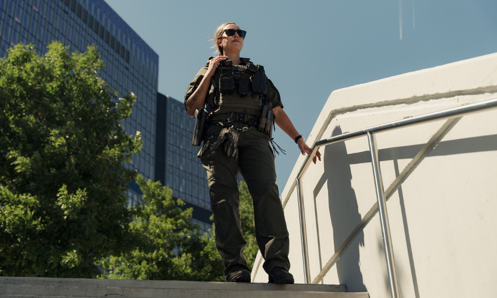 Tactical officer standing on an elevated structure in an urban environment, wearing operational gear and monitoring the surrounding area.