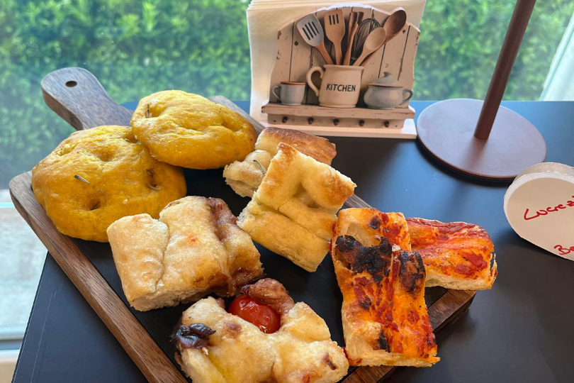 Tagliere con focaccine alla curcuma, focaccia con cipolle e pomodorini, pizza e focaccia bianca. 