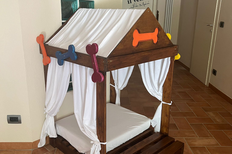 Camera Ascolano con letto matrimoniale sospeso, divano-letto, pavimento in resina e area vetrata che mostra le fondamenta del casale, soffitto in legno.